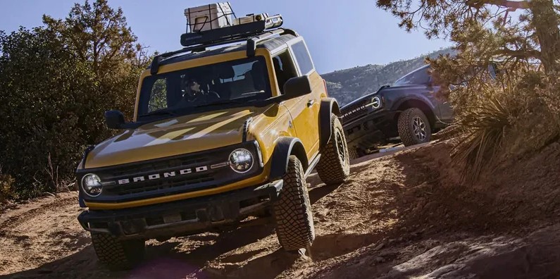 Brand new 2022 yellow / mustard Ford Bronco driving down sandy hillsides.