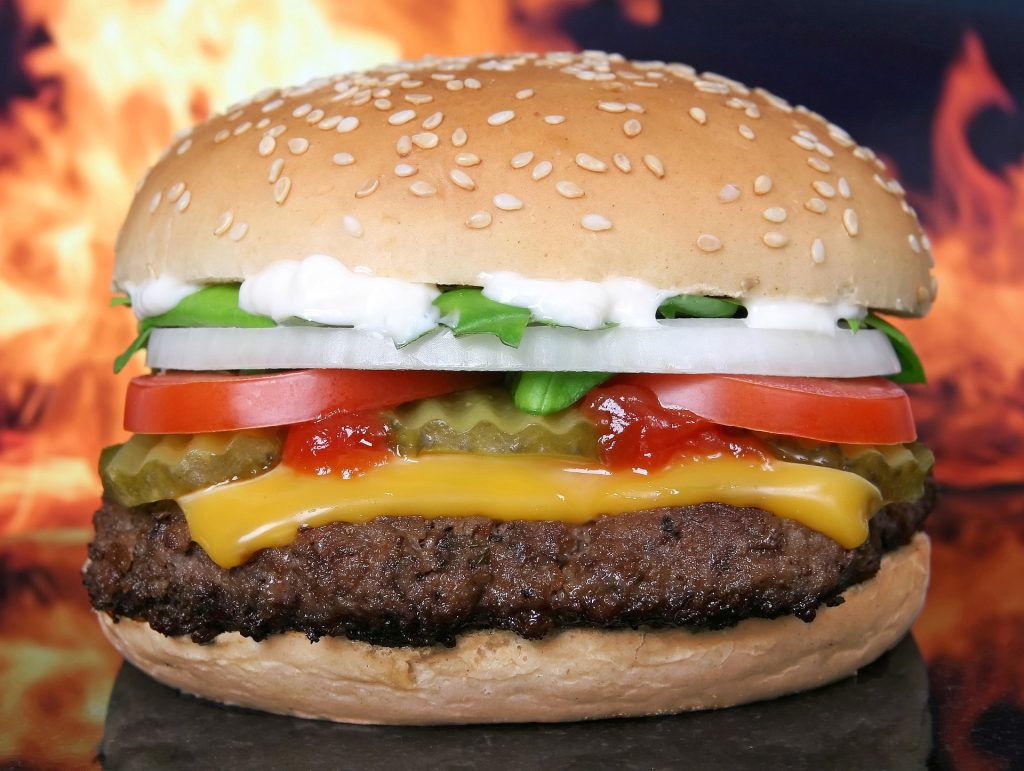 close up shot of a juicy burger with a lot of vibrant vegetables on it. Flames in the background