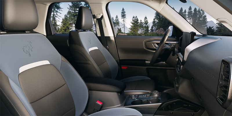 Interior of a 2025 Ford Bronco Sport SUV featuring gray and black seats with a modern design, surrounded by trees outside.